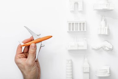 cropped view of man holding toy plane near statuettes from different countries of europe isolated on white  clipart