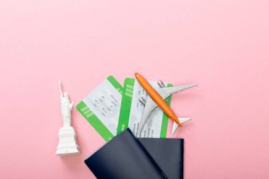 top view of air tickets near passports and small statue of liberty on pink  clipart