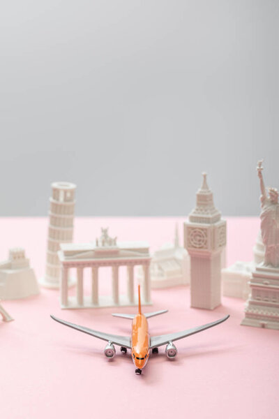 selective focus of toy airplane near small statuettes of different countries on grey and pink 