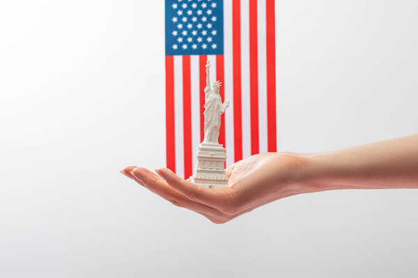 cropped view of woman holding small statue of liberty near american flag isolated on white 