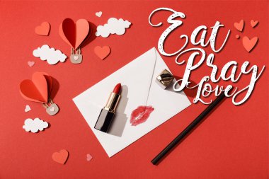 Kağıt bulutların ve kalp şeklindeki balonların üst görüntüsü, ruj ve kalem zarfın yanında dudak izi ve kırmızı arka planda aşk mektupları.