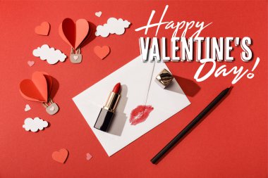 Kalp şeklindeki balonların üst görüntüsü, ruj ve kalem zarfın yanında dudak izi ve kırmızı arkaplanda mutlu sevgililer günü harfleri.