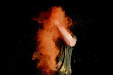 Siyah arka planda yüzünün önünde turuncu renkli holi boyalı bir kadın patladı.