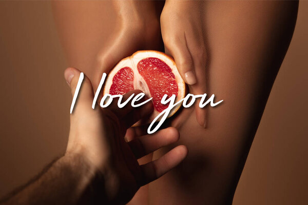Обрезанный вид мужчины, приближающегося к женщине в нейлоновых колготках, держащего пополам грейпфрут, рядом с которым я люблю тебя, опираясь на коричневый цвет
