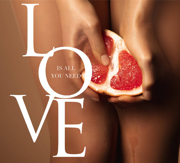 cropped view of woman in nylon tights holding grapefruit half near love is all you need lettering on brown