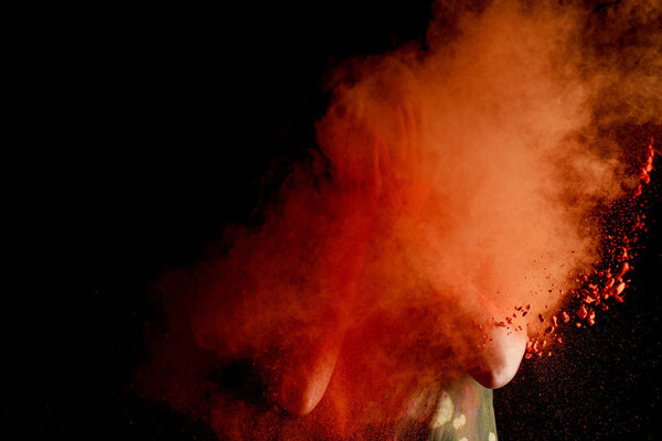 woman with orange colorful holi paint explosion in front of face on black background