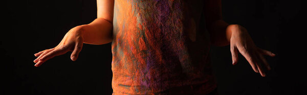 cropped view of woman with orange colorful holi paint powder on body and clothes isolated on black, panoramic shot