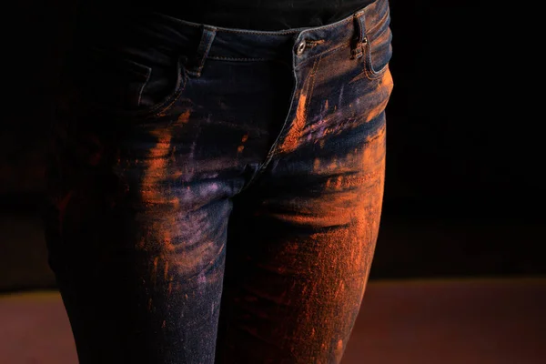 黒を基調としたジーンズにオレンジのカラフルなホリペイントパウダーを持つ女性のクロップドビュー — ストック写真