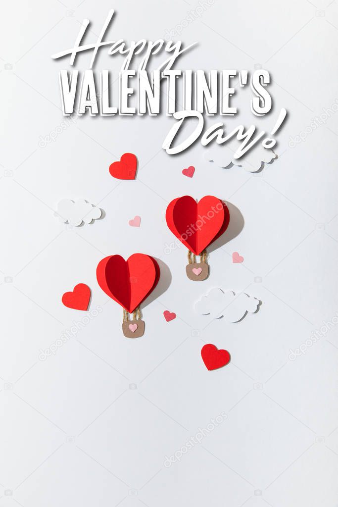top view of paper heart shaped air balloons in clouds near happy valentines day lettering on white background