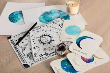 Selective focus of birth chart and cards with watercolor drawings of moon phases and candle on table clipart