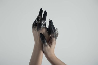 Cropped view of hand of witch in black paint with jewelry rings isolated on grey  clipart