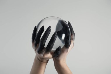 Cropped view of black painted hands of witch holding crystal ball isolated on grey clipart