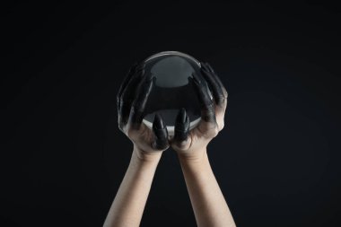 Cropped view of witch hands in black dye holding crystal ball isolated on black clipart