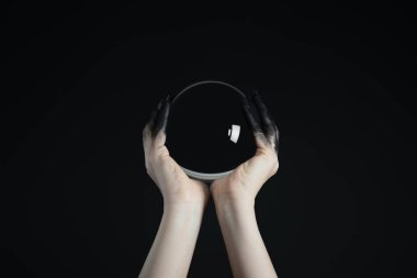 Cropped view of witch holding crystal ball in black painted hands isolated on black clipart