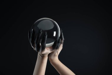 Cropped view of witch with black paint on hands holding crystal ball isolated on black clipart