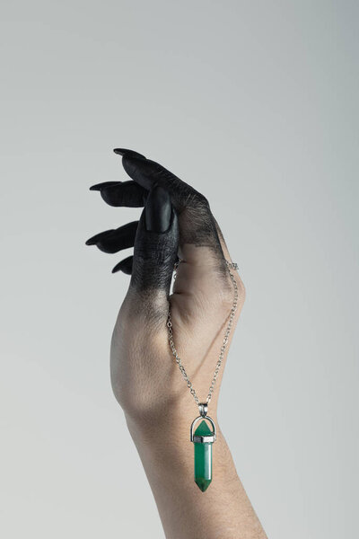 Cropped view of black painted witch hand holding crystal on chain isolated on grey 