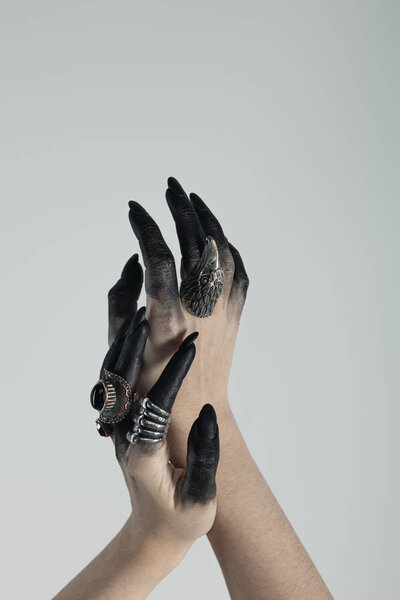 Cropped view of witch hands with black dye and jewelry rings isolated on grey 