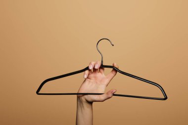 cropped view of woman holding empty hanger isolated on beige clipart