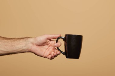 cropped view of man holding black mug isolated on beige clipart