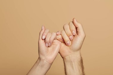 cropped view of man and woman holding little fingers isolated on beige clipart