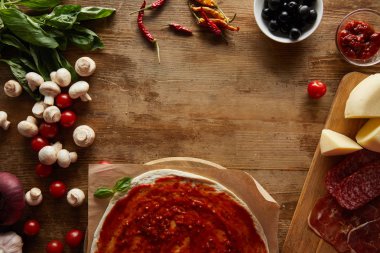 Top view of pizza and ingredients around on wooden background