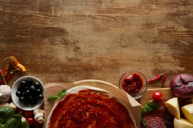 Top view of pizza on parchment paper with ingredients on wooden background