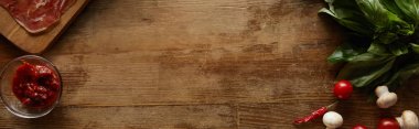 Top view of ingredients for pizza including tomato sauce, mushrooms, cherry tomatoes, chili peppers and prosciutto on wooden background, panoramic shot