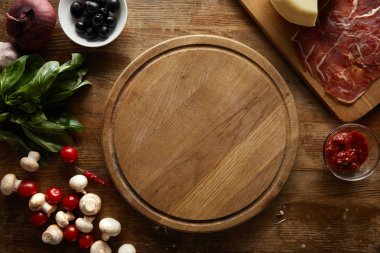 Top view of ingredients for pizza around cutting board on wooden background