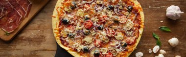 Top view of tasty pizza and garlic, prosciutto, mushrooms and basil on wooden background, panoramic shot