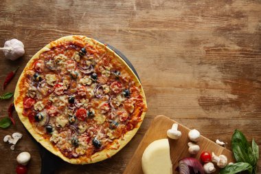 Top view of pizza and vegetables on wooden background