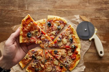 Cropped view of man holding piece of pizza on wooden background