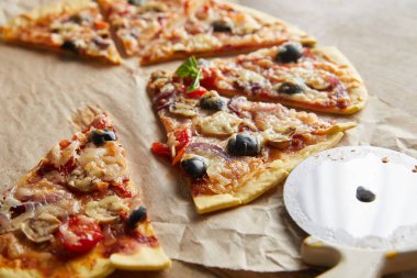 Kesilmiş lezzetli İtalyan pizzası, zeytinli ekmek kağıdı, pizza bıçağı ve ahşap masa.