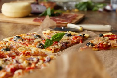 Lezzetli İtalyan pizzasının seçici odak noktası zeytinli, malzemelerin yanında ekmek kağıdı ve ahşap masada pizza bıçağı.