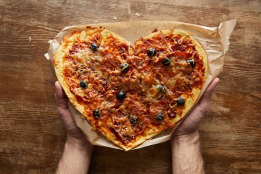Kalbinde lezzetli İtalyan pizzası taşıyan adamın kısmi görüntüsü ahşap masada kağıt üzerinde.