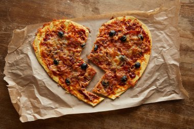 Lezzetli İtalyan pizzasının üst görüntüsü kırık kalp şeklinde ahşap masadaki kağıt fırınında