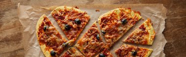 Lezzetli kalp şeklinde İtalyan pizzası ahşap masa üzerinde kağıt parçalarına ayrılmış, panoramik çekim.