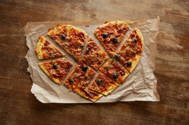 Lezzetli İtalyan pizzasının kalp şeklinde ahşap masada kağıt parçalarına ayrılmış görüntüsü.