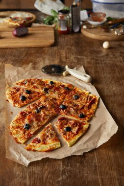 Lezzetli İtalyan pizzası kalp şeklinde. Tahta masada pizza bıçağının yanında kağıt parçalarıyla dilimlenmiş.