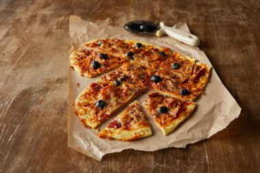 Lezzetli İtalyan pizzası kalp şeklinde. Tahta masada pizza bıçağının yanında kağıt parçalarıyla dilimlenmiş.