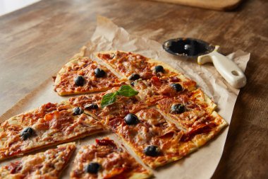 Lezzetli İtalyan pizzası kalp şeklinde. Tahta masada pizza bıçağının yanında kağıt parçalarıyla dilimlenmiş.
