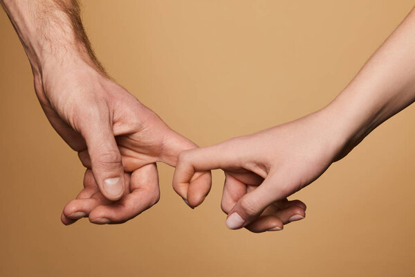 cropped view of man and woman holding fingers isolated on beige