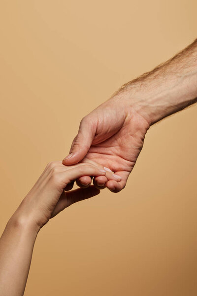 cropped view of man holding woman hand isolated on beige
