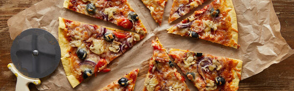 вид сверху на срезанную вкусную итальянскую пиццу с оливками на выпечке бумаги рядом с ножом для пиццы на деревянном фоне, панорамный снимок
