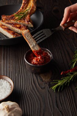 Domates sosuna sarımsak ve tuz koyarak ahşap yüzeye biftek dilimi koyan kadın manzarası.