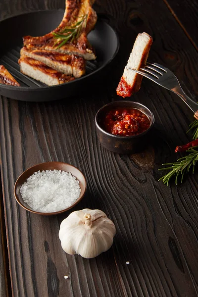 Selective focus of fork with steak slice by tomato sauce with salt and garlic on wooden surface — Stock Image Selective Focus Fork Steak Slice Tomato Sauce Salt Garlic Wooden Stock Image