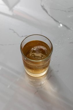 top view of glass with whiskey and ice cube on white marble surface  clipart