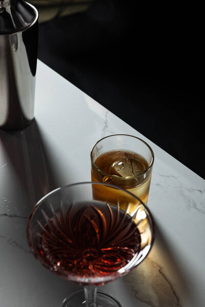 selective focus of glass with whiskey near red wine and shaker isolated on black 