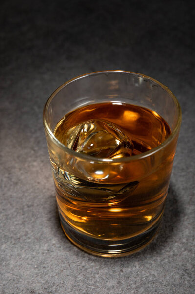 ice cubes in glass of alcoholic drink on grey surface 