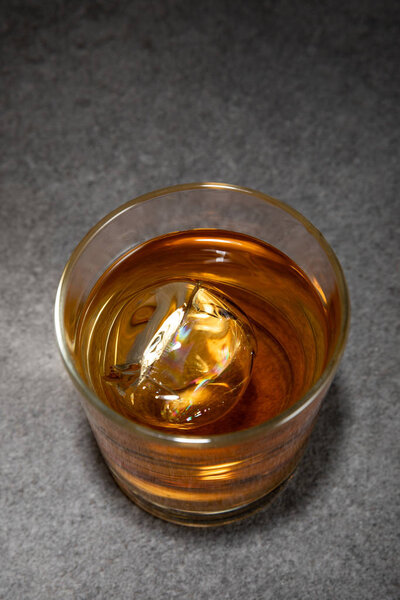 top view of frozen ice cube in glass of brandy on grey surface 