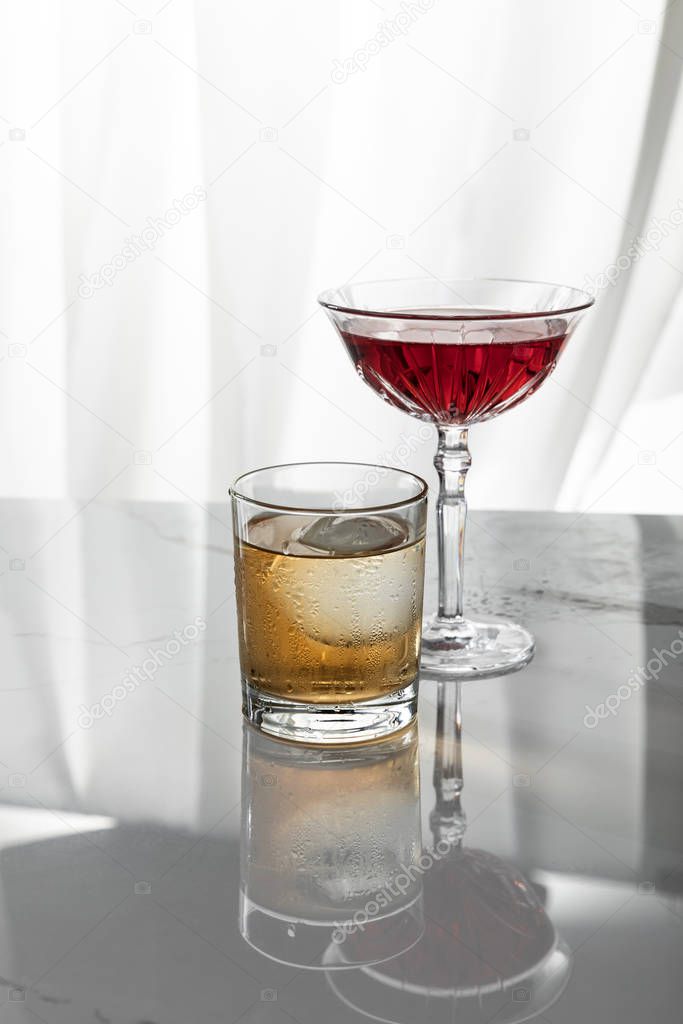 red wine near glass of whiskey on white 
